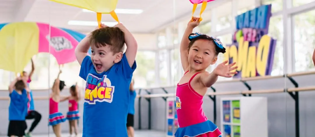Two preschoolers laughing and dancing under a play parachute in a Ready Set Dance class